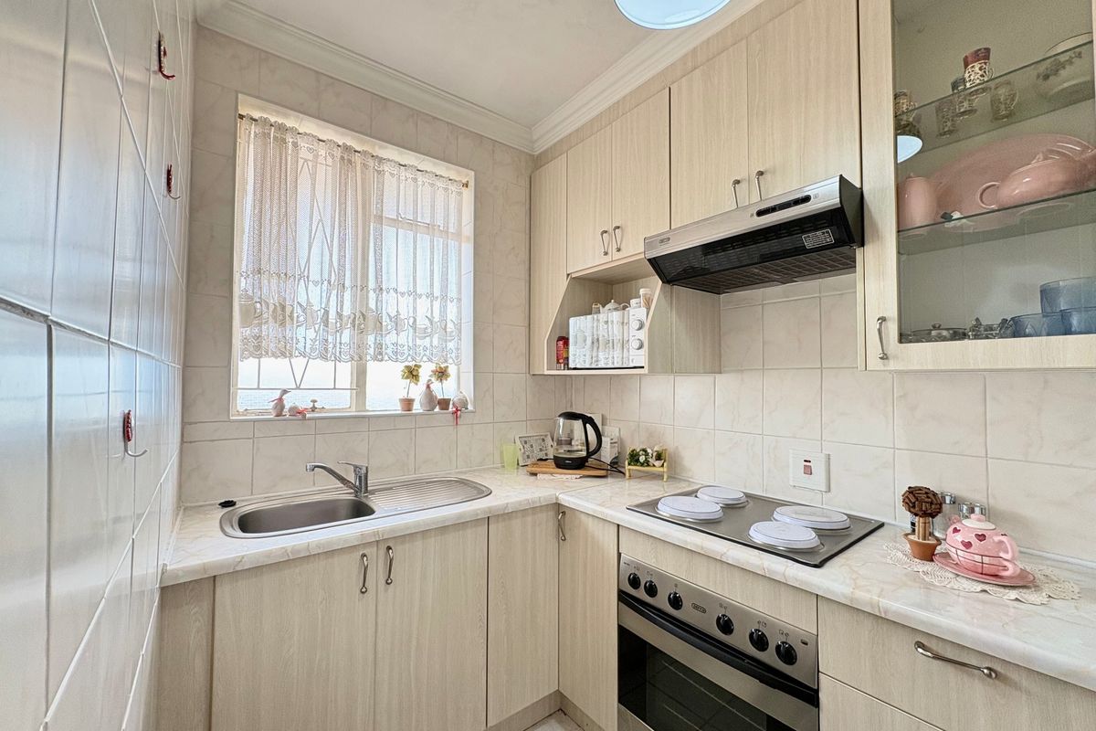 A functional kitchen featuring light wood-finish cabinetry, laminate countertops, a built-in oven with electric hob, and tiled splashbacks.