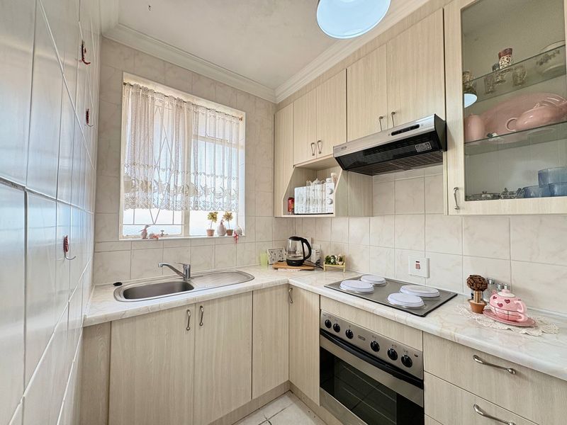 A functional kitchen featuring light wood-finish cabinetry, laminate countertops, a built-in oven with electric hob, and tiled splashbacks.