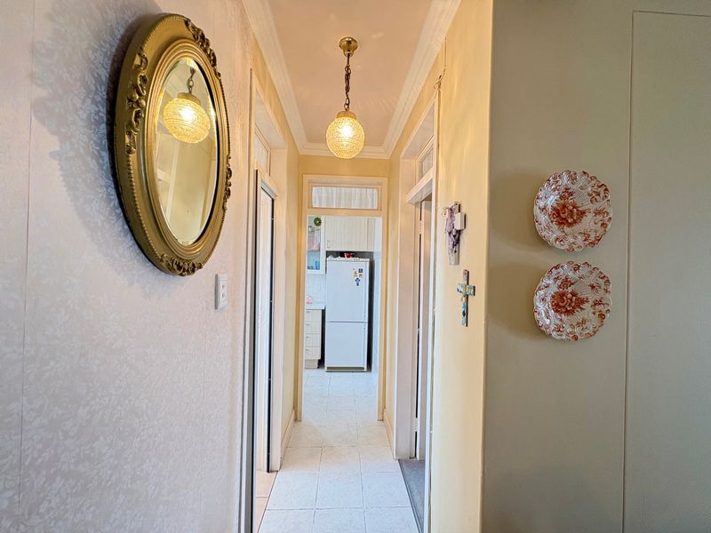 A bright hallway featuring tiled flooring, decorative coving, and a pendant light fixture, providing access to adjacent rooms and a view into the kitchen.