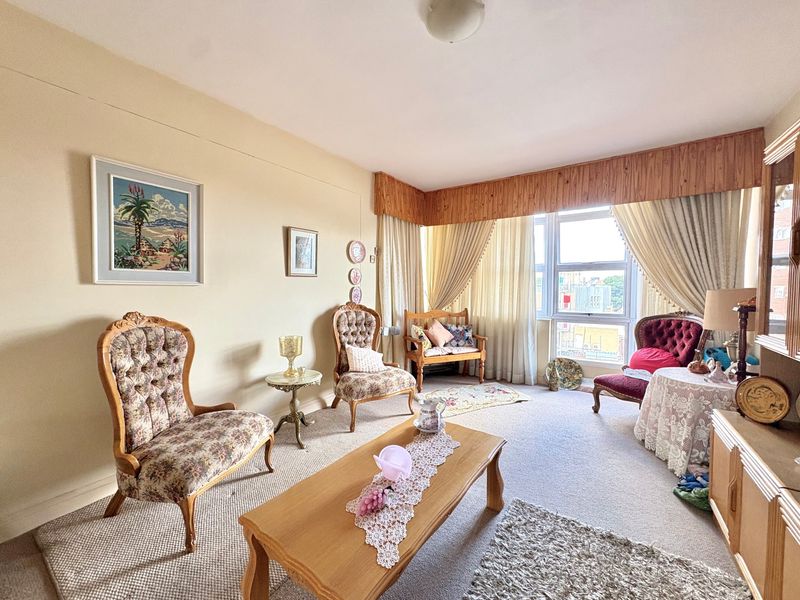 A living room featuring a large window with a wooden pelmet and neutral wall finishes, offering a bright and traditional living space.