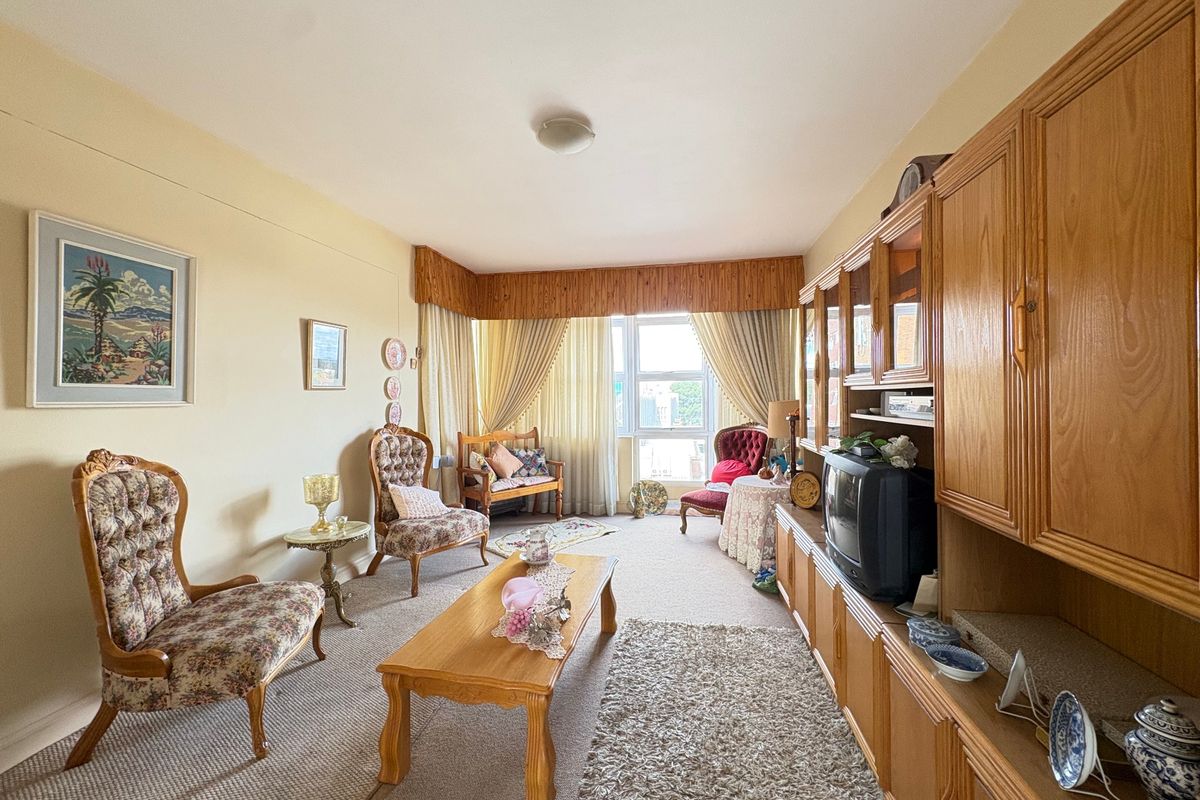 A living room featuring carpet flooring, a large window with curtains, and extensive built-in wooden cabinetry along one wall.