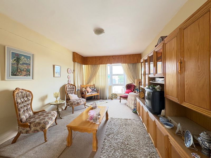 A living room featuring carpet flooring, a large window with curtains, and extensive built-in wooden cabinetry along one wall.