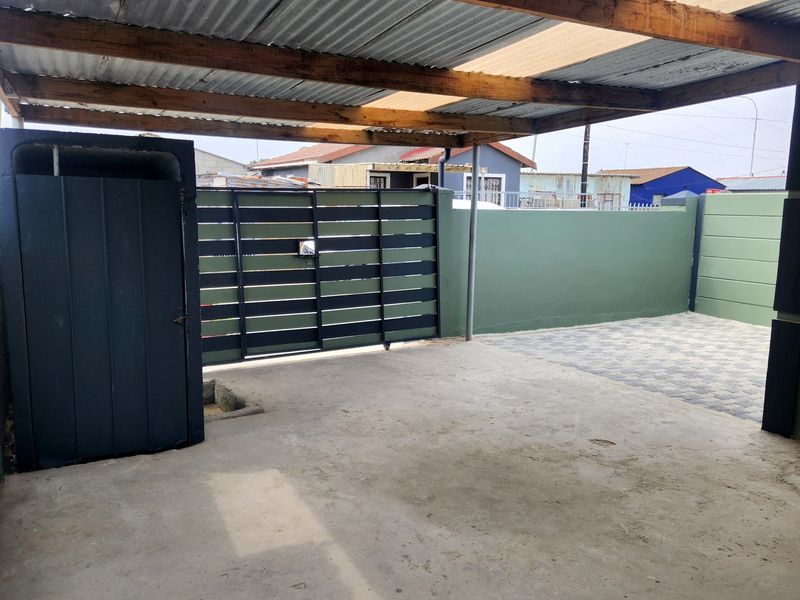 A covered outdoor parking area featuring a corrugated metal roof, concrete flooring, and secure boundary walls with a metal gate.