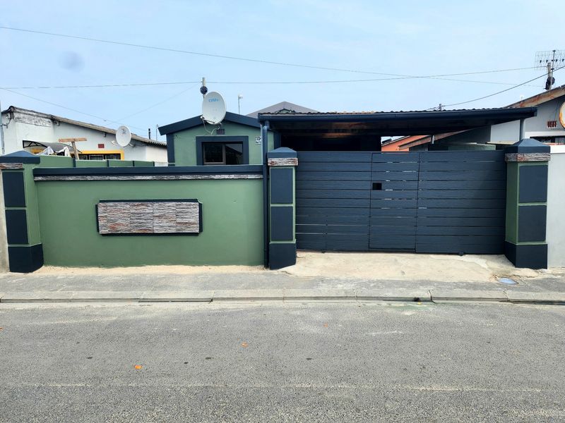 Front elevation of the property featuring a secure boundary wall with stone cladding accents and a private gated driveway with a carport.