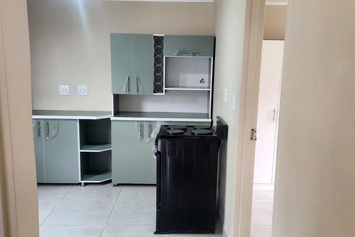 A clean, functional kitchen featuring modern light green cabinetry, tiled flooring, and a black freestanding stove, presented in a bright, neutral space.