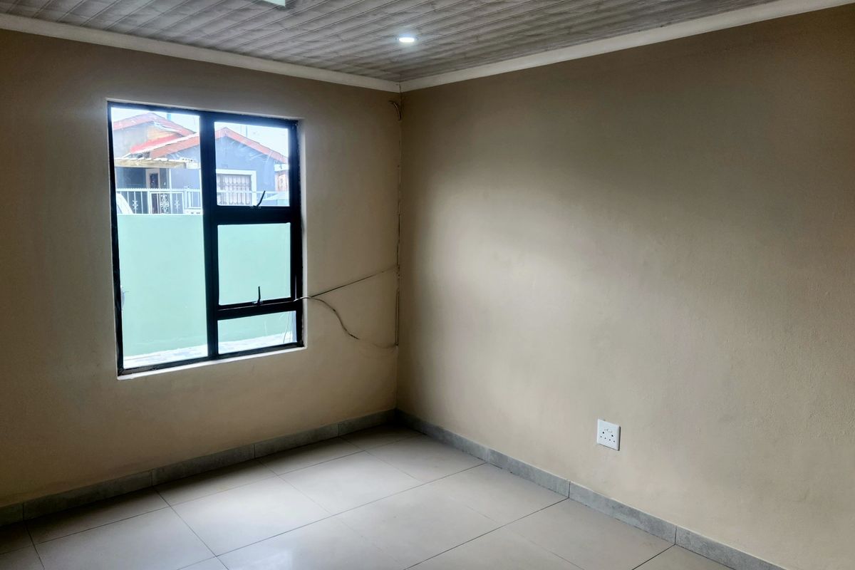 An empty bedroom featuring tiled flooring, recessed downlights, and an aluminium window frame. The space is ready for personalization.