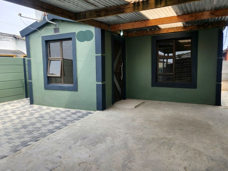 Front exterior view of the house featuring a covered patio area, paved driveway, and modern green facade with dark trim detailing.