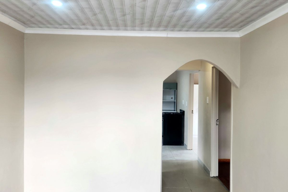 A bright, empty living area featuring neutral walls, tiled flooring, and a distinctive arched doorway leading to an adjacent space.