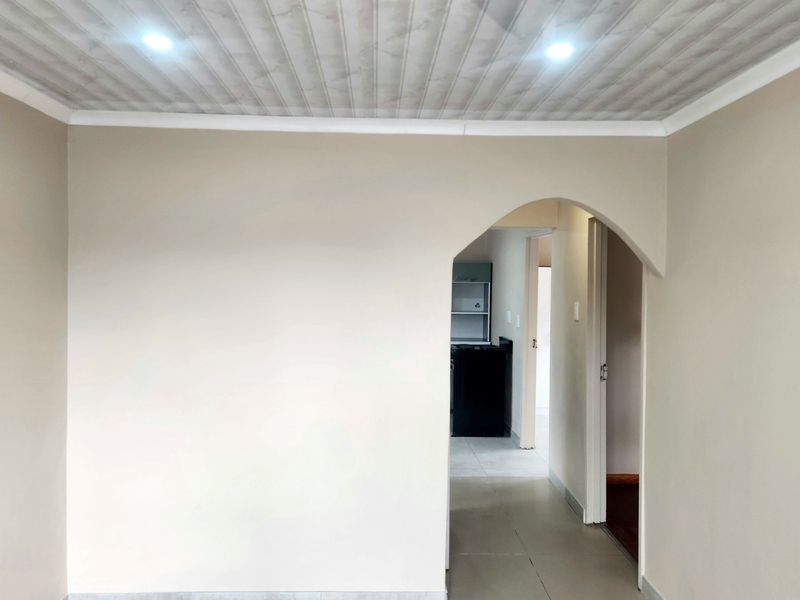A bright, empty living area featuring neutral walls, tiled flooring, and a distinctive arched doorway leading to an adjacent space.