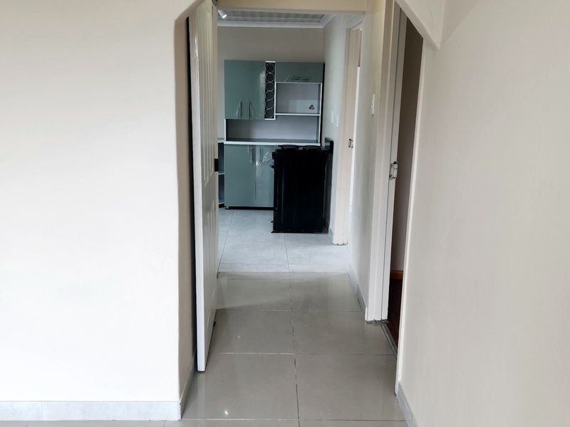 A view through an arched doorway into a hallway leading to a kitchen area with tiled flooring and modern cabinetry.