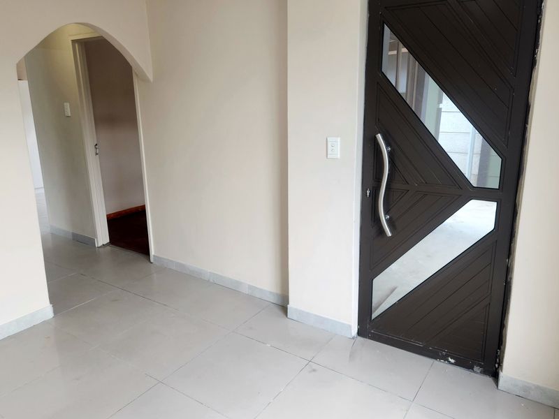 An empty entrance hall featuring tiled flooring, a decorative front door with glass inserts, and an arched transition to the interior living space.