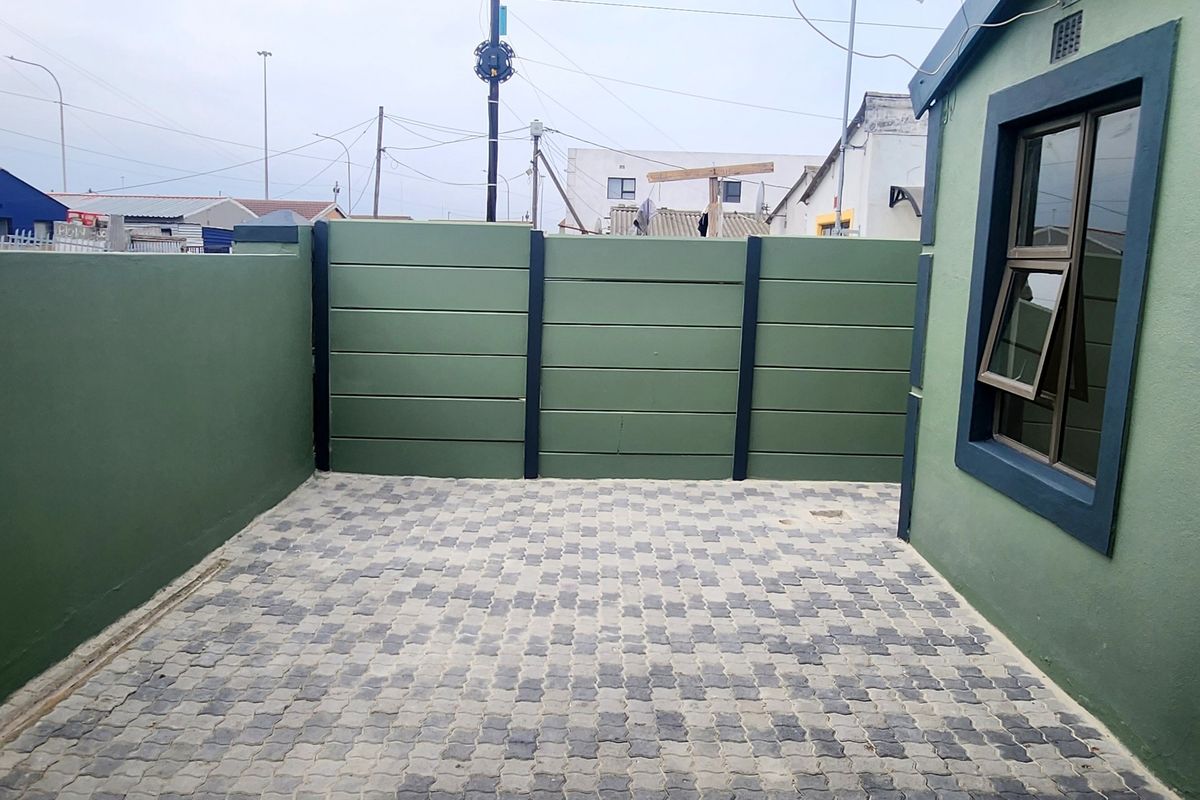 A neat, paved rear courtyard area enclosed by a painted precast concrete boundary wall, featuring a modern aluminium window frame.