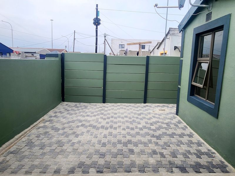 A neat, paved rear courtyard area enclosed by a painted precast concrete boundary wall, featuring a modern aluminium window frame.