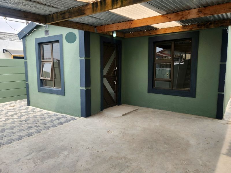 Front exterior view of the house featuring a covered patio area, paved driveway, and modern aluminium window frames.