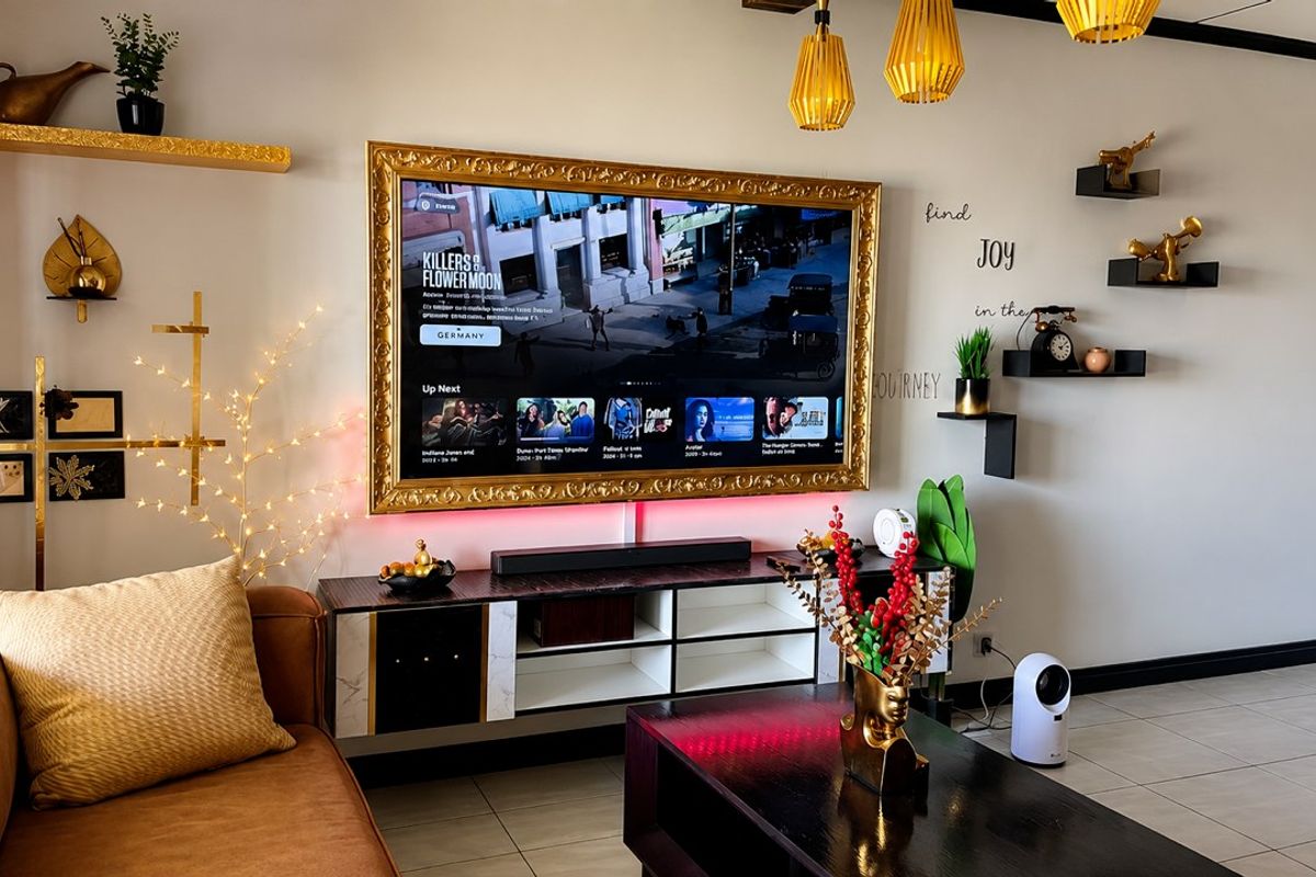 A well-maintained living room featuring tiled flooring, modern pendant lighting, and a wall-mounted television with decorative framing.
