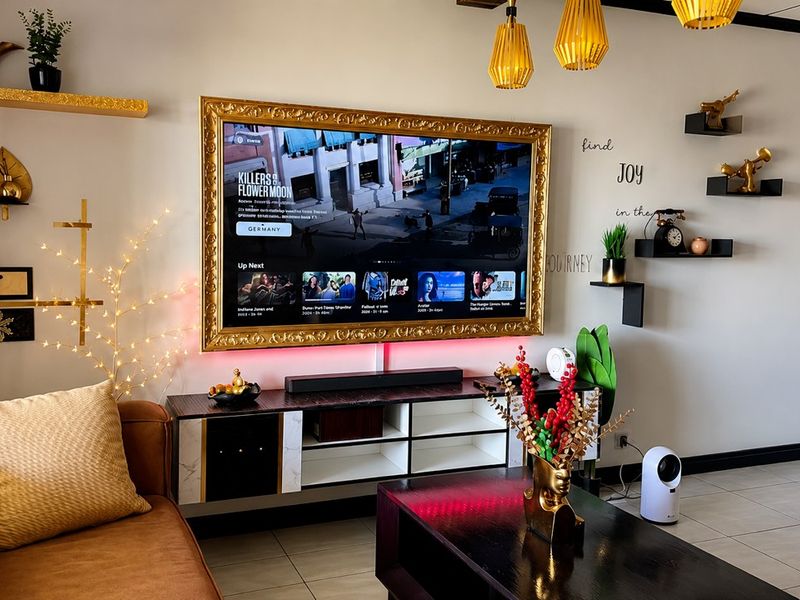 A well-maintained living room featuring tiled flooring, modern pendant lighting, and a wall-mounted television with decorative framing.