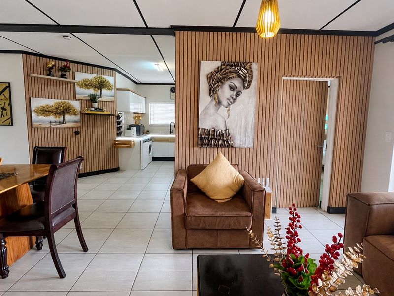 Open-plan living and kitchen area featuring modern slatted wood wall paneling, neutral ceramic floor tiles, and a functional kitchen layout.