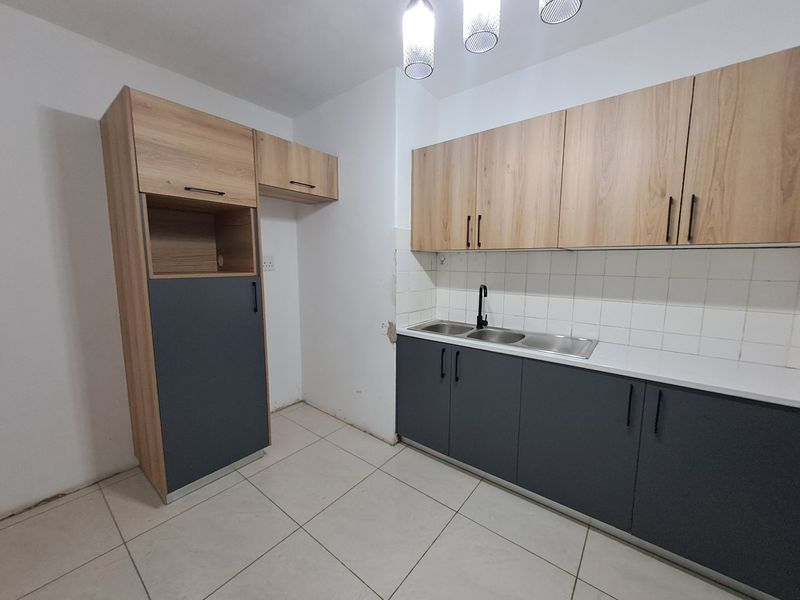 A functional kitchen featuring modern two-tone cabinetry, a double sink, tiled backsplash, and neutral floor tiles, offering a clean canvas for personalization.