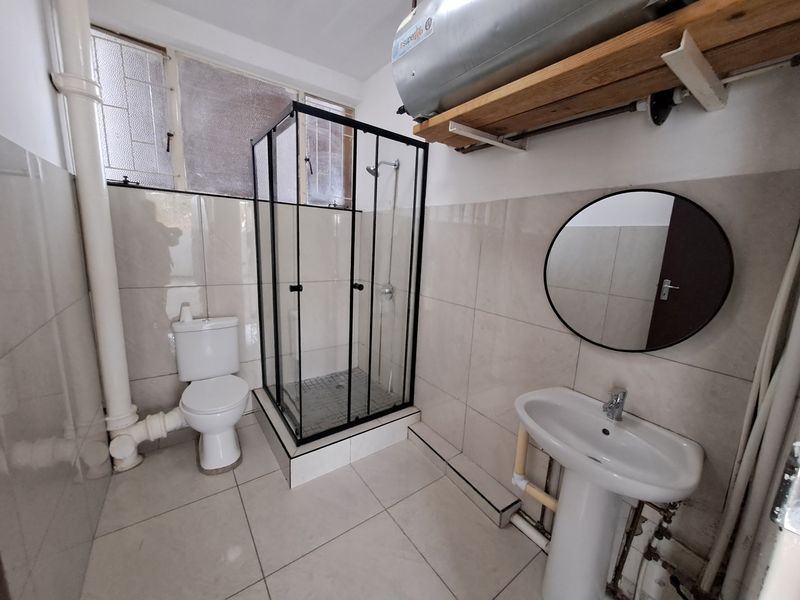 A functional bathroom featuring a shower enclosure, pedestal basin, toilet, and wall-mounted electric water heater with tiled finishes throughout.