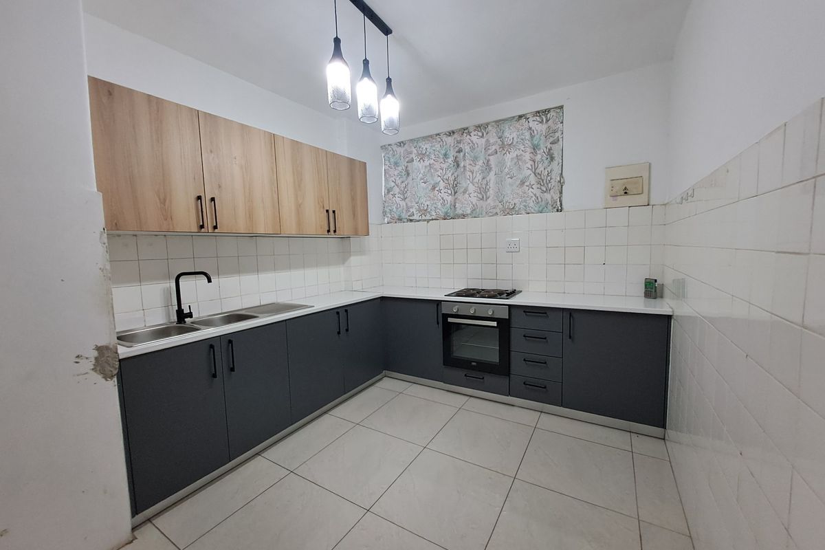 A functional kitchen featuring two-tone cabinetry, built-in oven and hob, tiled backsplash, and neutral floor tiles, offering a clean and practical workspace.