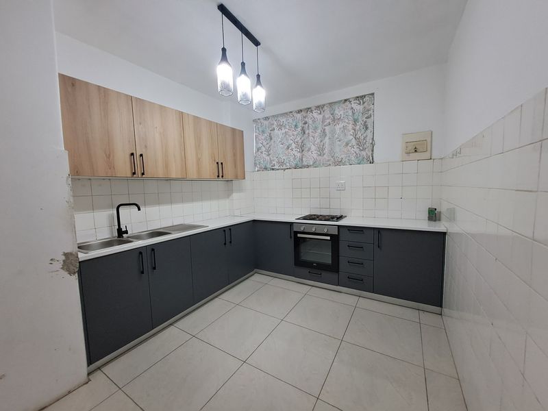 A functional kitchen featuring two-tone cabinetry, built-in oven and hob, tiled backsplash, and neutral floor tiles, offering a clean and practical workspace.