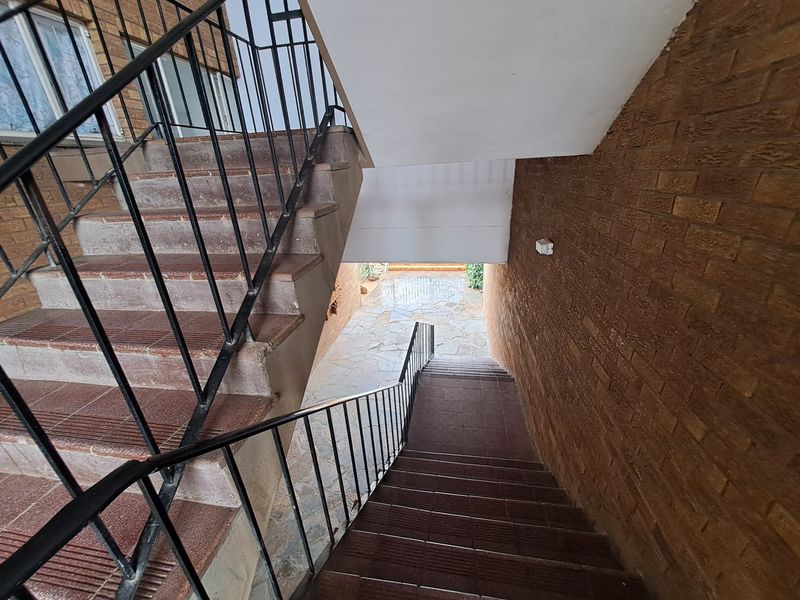 An outdoor-facing stairwell featuring brick walls, tiled steps, and metal balustrades leading to a paved ground level area.