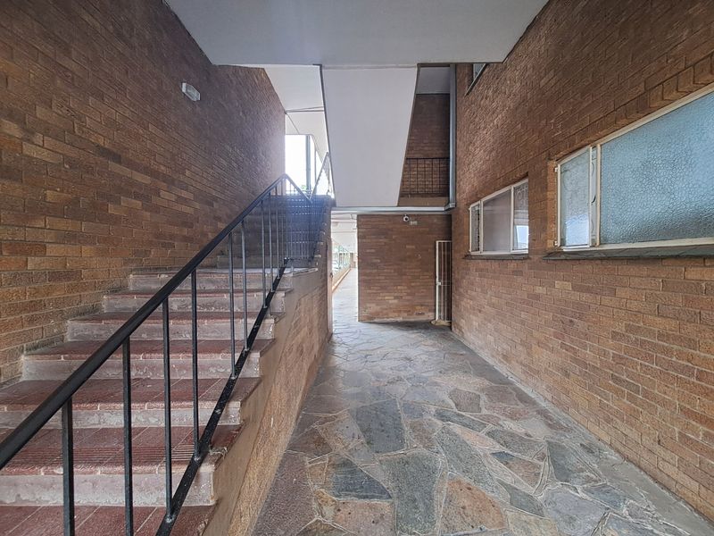 An exterior apartment building entrance featuring brick walls, stone flooring, and a tiled staircase with a metal handrail.