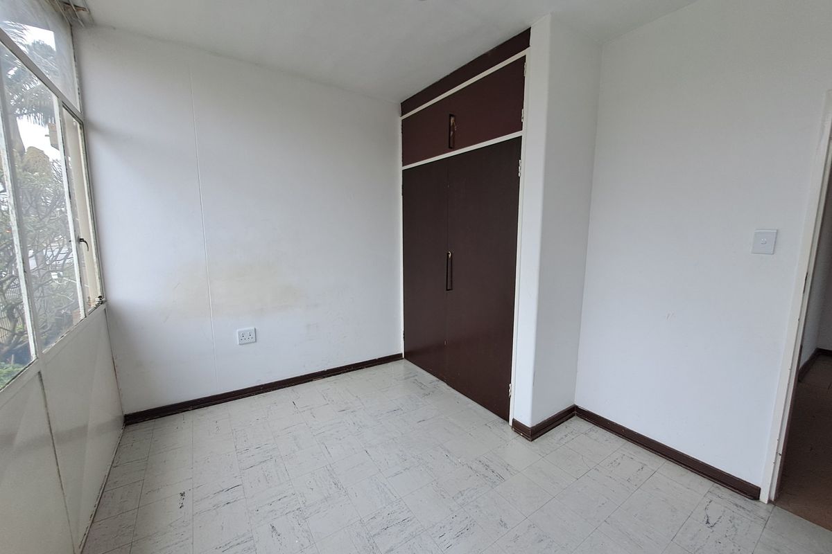 An empty bedroom featuring built-in cupboards, vinyl tile flooring, and large windows, presenting a blank canvas for renovation or staging.