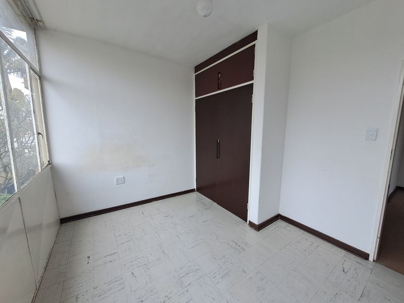 An empty bedroom featuring built-in cupboards, vinyl tile flooring, and large windows, presenting a blank canvas for renovation or staging.