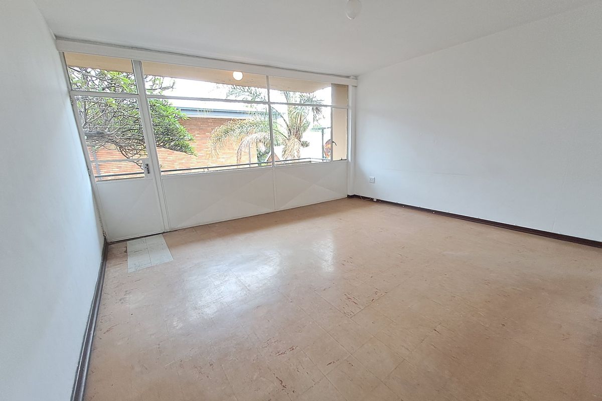 An empty living room featuring large glass doors leading to a balcony, with neutral walls and worn vinyl flooring throughout.