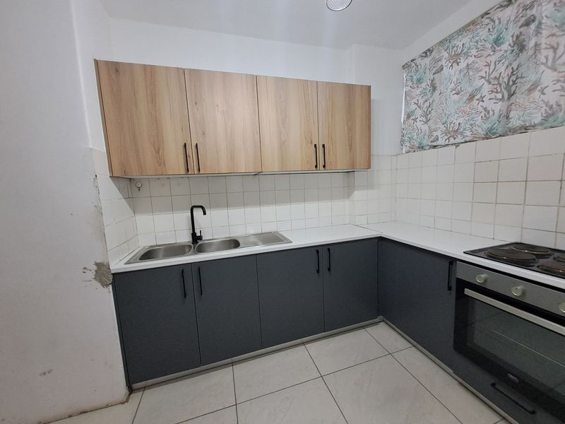 A functional kitchen featuring modern two-tone cabinetry, a double sink with a black tap, built-in oven, and hob, with tiled backsplash and flooring.