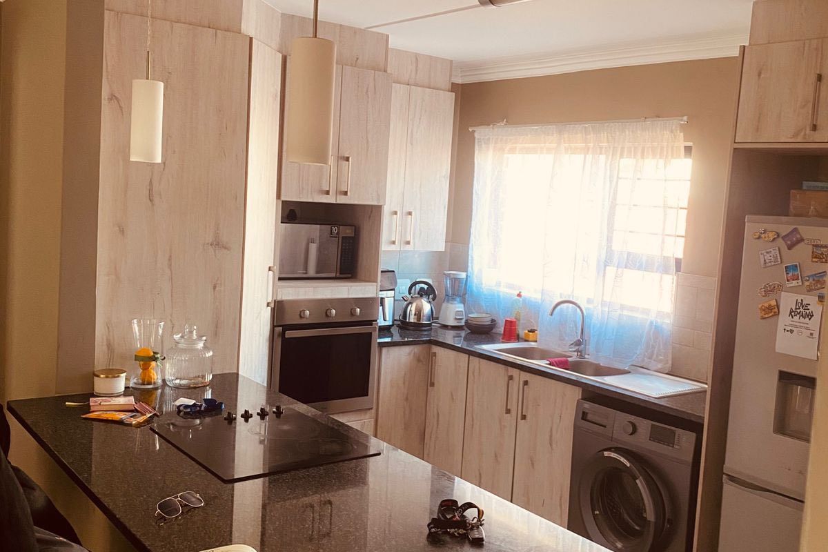 A functional kitchen featuring light wood-finish cabinetry, dark granite countertops, a built-in oven and hob, and tiled flooring.