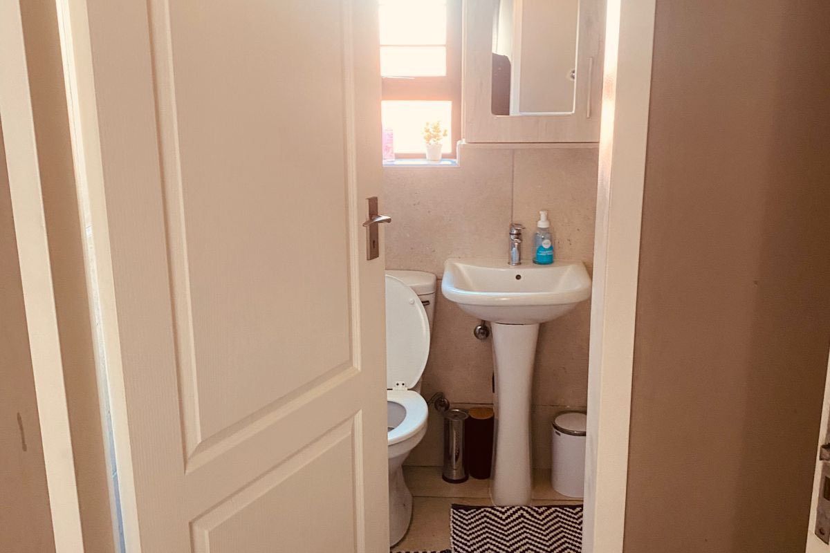 A compact bathroom featuring a pedestal sink, toilet, and wall-mounted medicine cabinet with neutral tiled flooring and natural light from a window.