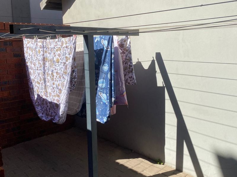A functional outdoor laundry area featuring a fixed washing line, paved flooring, and a brick boundary wall.