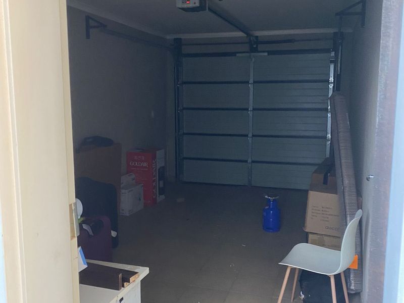 A functional single-car garage featuring tiled flooring, a sectional door with an automatic opener, and overhead fluorescent lighting.