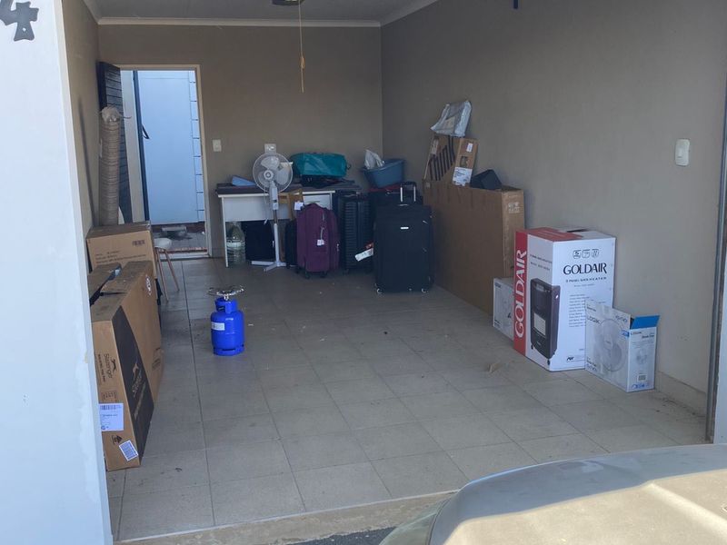 A functional single-car garage featuring tiled flooring, overhead lighting, and a side access door, currently used for storage.
