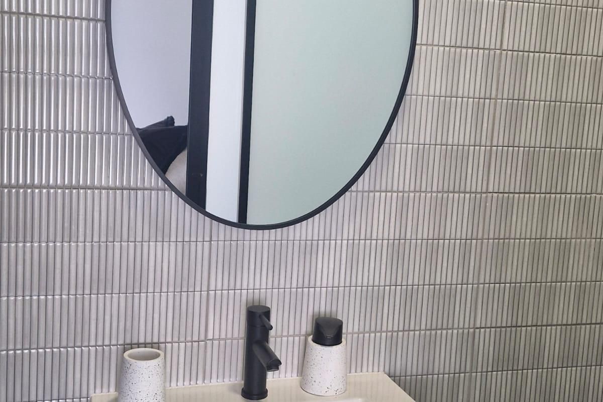 Modern bathroom vanity featuring a sleek black mixer tap, integrated basin, and a stylish round mirror set against contemporary vertical finger tiles.