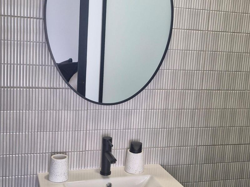 Modern bathroom vanity featuring a sleek black mixer tap, integrated basin, and a stylish round mirror set against contemporary vertical finger tiles.