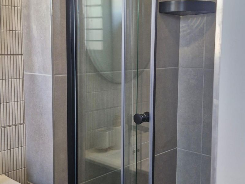 Modern bathroom featuring a sleek shower enclosure with black framing, contemporary grey wall tiling, and a built-in corner shelf.