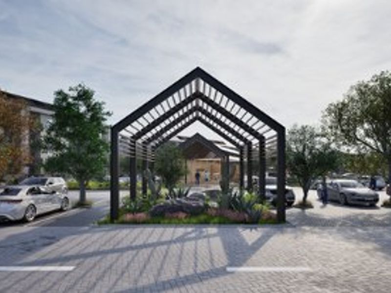 A modern apartment complex entrance featuring a striking architectural pergola, landscaped garden beds, and paved parking area.