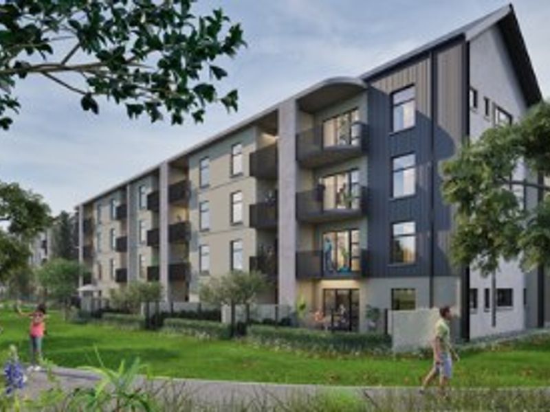 A modern multi-story apartment building featuring private balconies, a pitched roof design, and well-maintained landscaped garden areas with paved walkways.