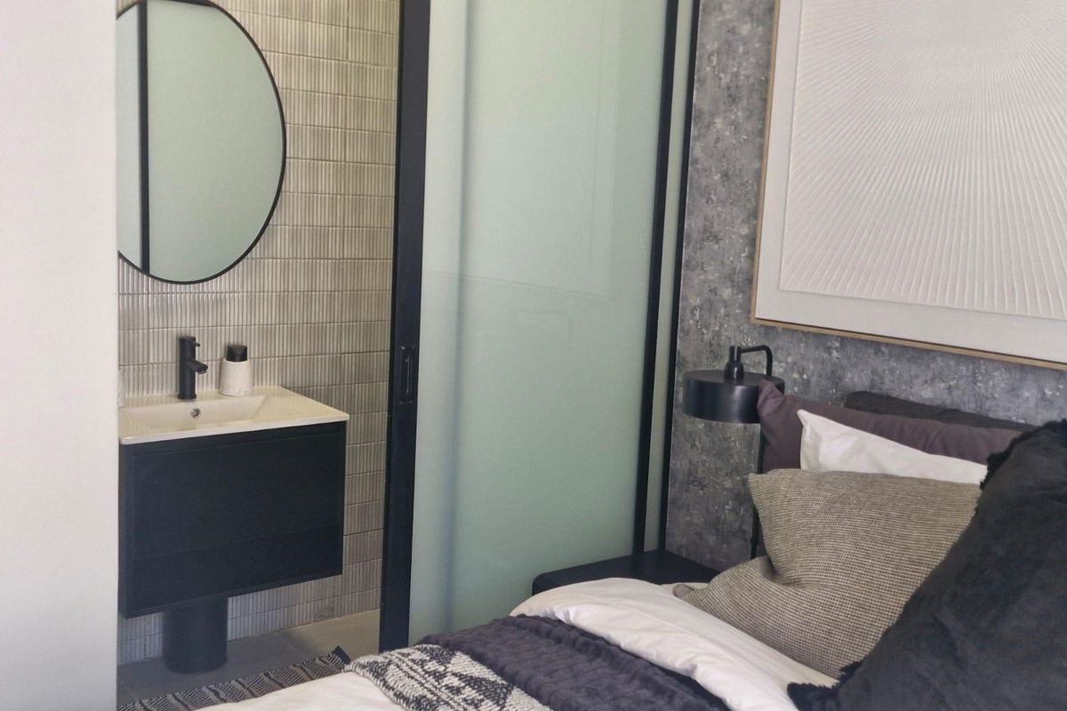 A modern bedroom featuring a sleek wall-mounted vanity with a basin and round mirror, separated from the sleeping area by a sliding glass door.