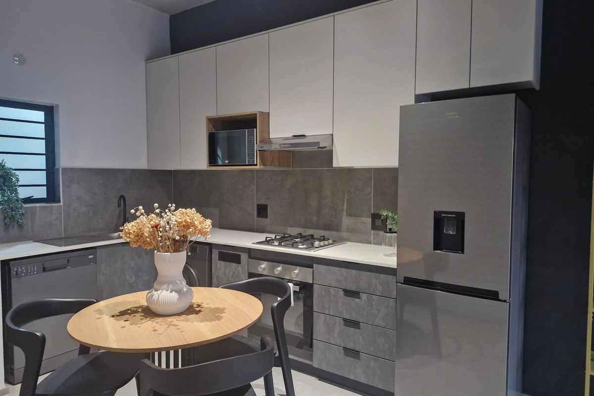 Modern kitchen featuring sleek grey and white cabinetry, stone countertops, integrated appliances, and a gas hob with a stylish tiled backsplash.