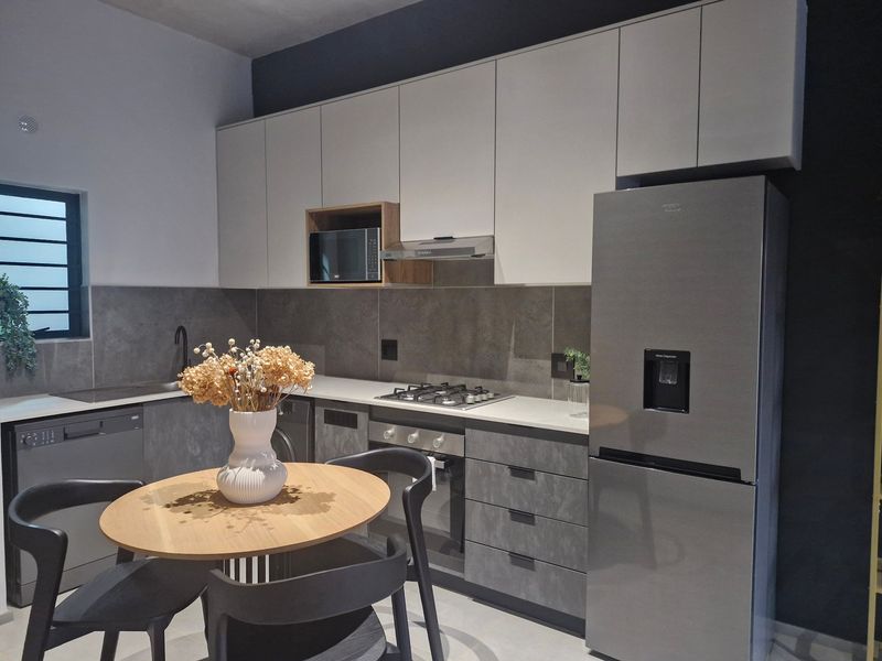 Modern kitchen featuring sleek grey and white cabinetry, stone countertops, integrated appliances, and a gas hob with a stylish tiled backsplash.