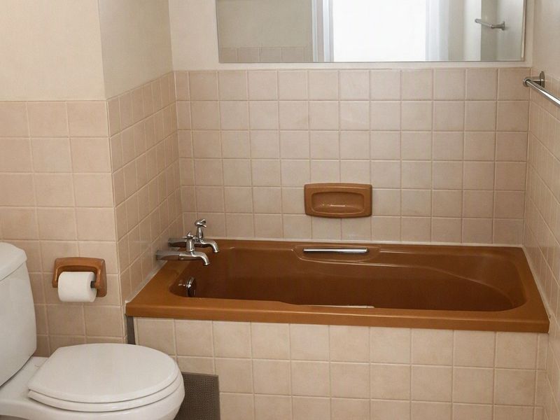 A functional bathroom featuring a built-in bathtub, toilet, and wall-mounted mirror with neutral tiled finishes.