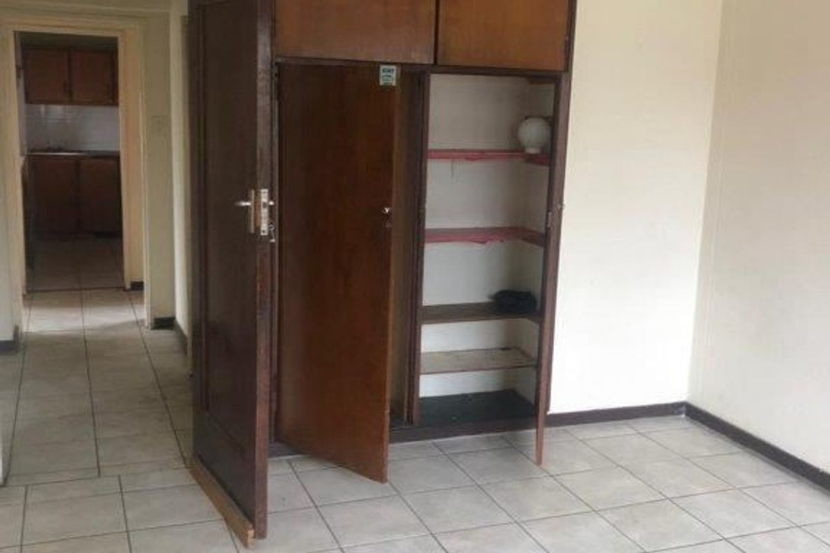 An empty bedroom featuring ceramic floor tiles and a dated built-in wooden wardrobe with overhead storage compartments.
