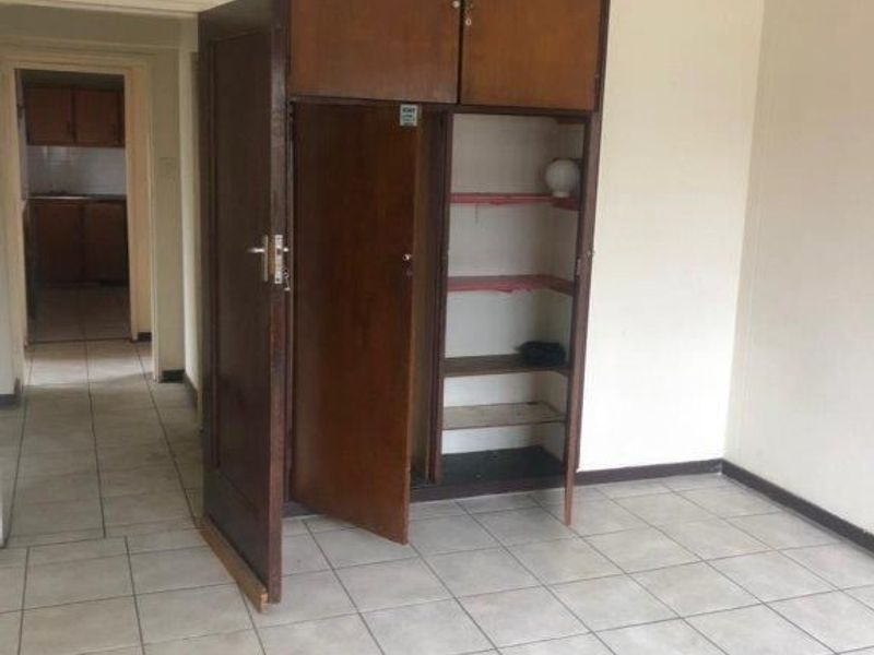 An empty bedroom featuring ceramic floor tiles and a dated built-in wooden wardrobe with overhead storage compartments.