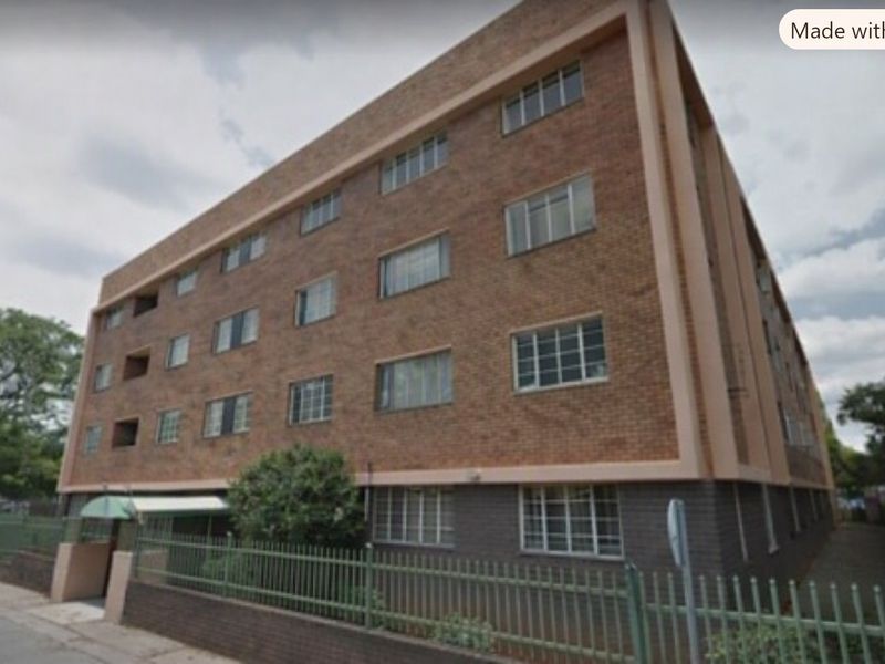 A multi-story brick apartment building exterior featuring metal-framed windows and a perimeter fence at the street level.