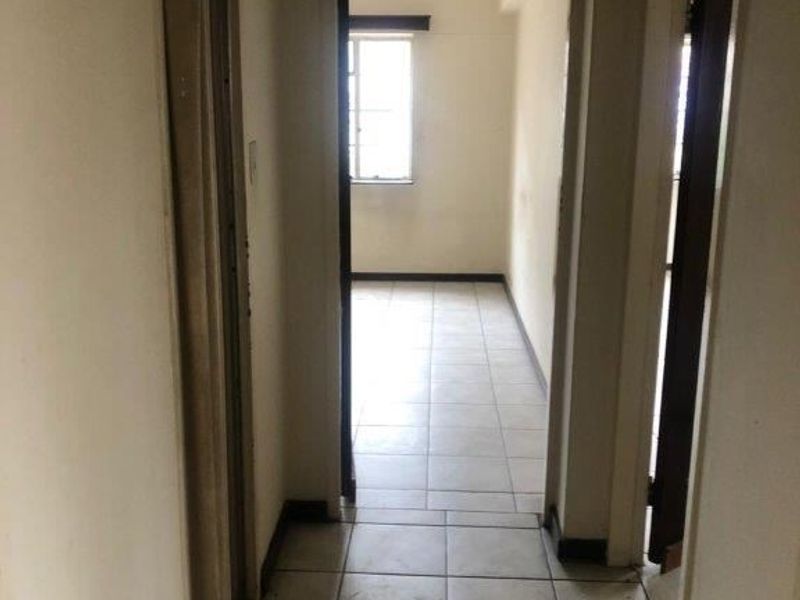 A narrow interior hallway featuring tiled flooring and access to adjacent rooms, showing signs of wear and requiring cosmetic updates.