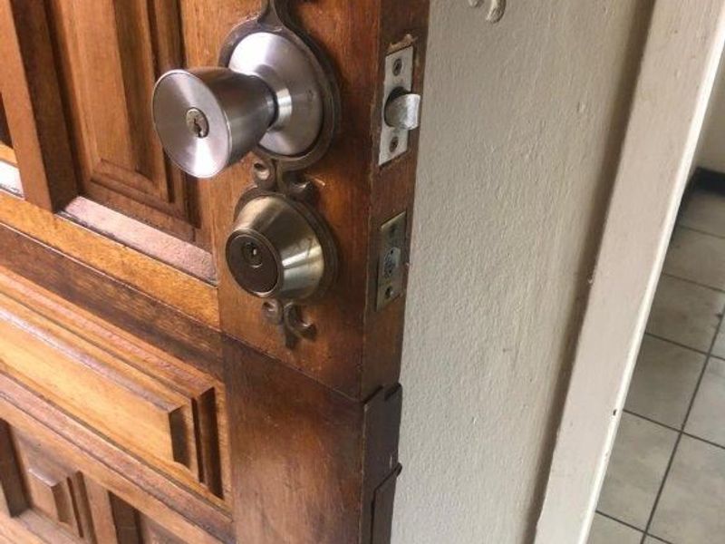 Close-up view of a solid wood entry door featuring a metal handle and deadbolt lock, with visible wear on the door and adjacent wall.